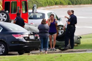 A woman talks on the phone next to a car accident.