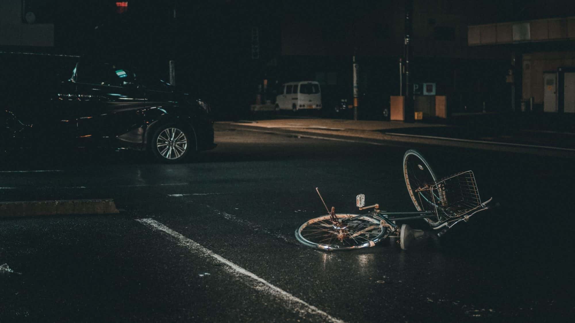 A damaged bike lies in the middle of the road, a dented van is parked nearby.
